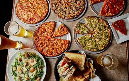 A dinner table full of 5 pizzas, a salad, and sandwiches at Cape Cod Cafe.